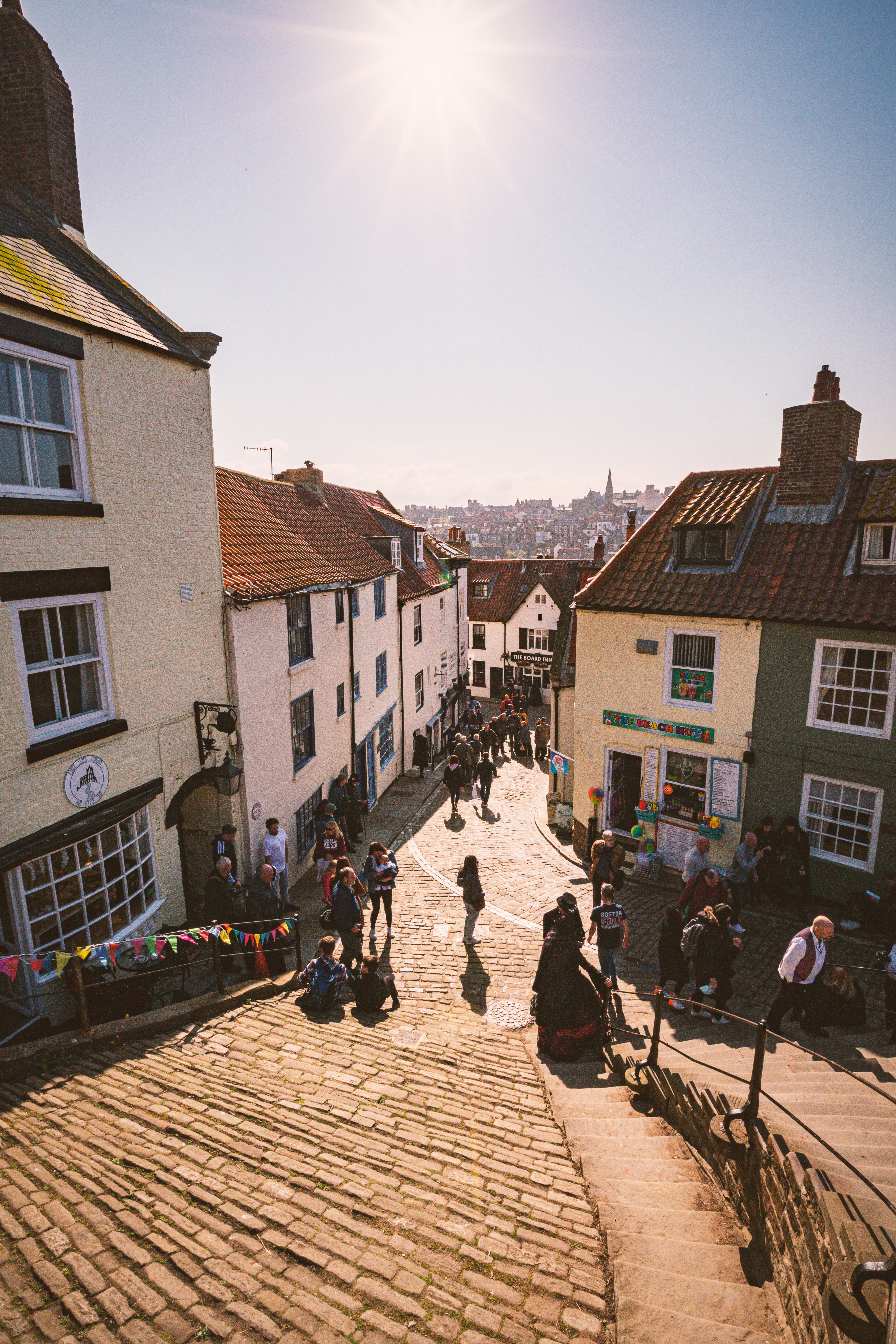 Visitors walking down Whitby&rsquo;s cobbled Church Street towards the harbour in North Yorkshire on a sunny day